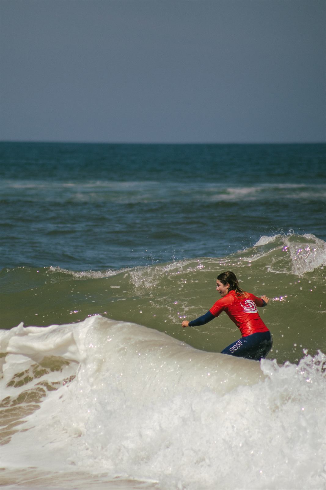 Aluna a atravessar a espuma numa aula de surf