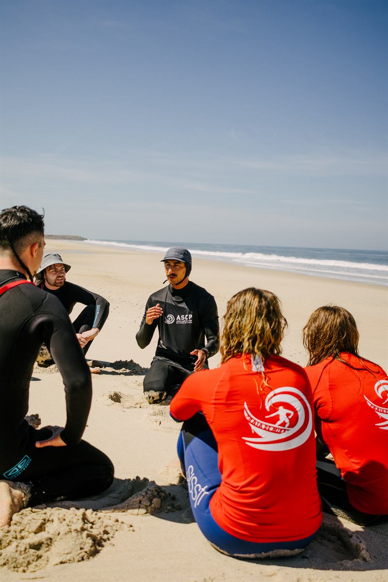 Instrutor em briefing com alunos na areia antes da aula
