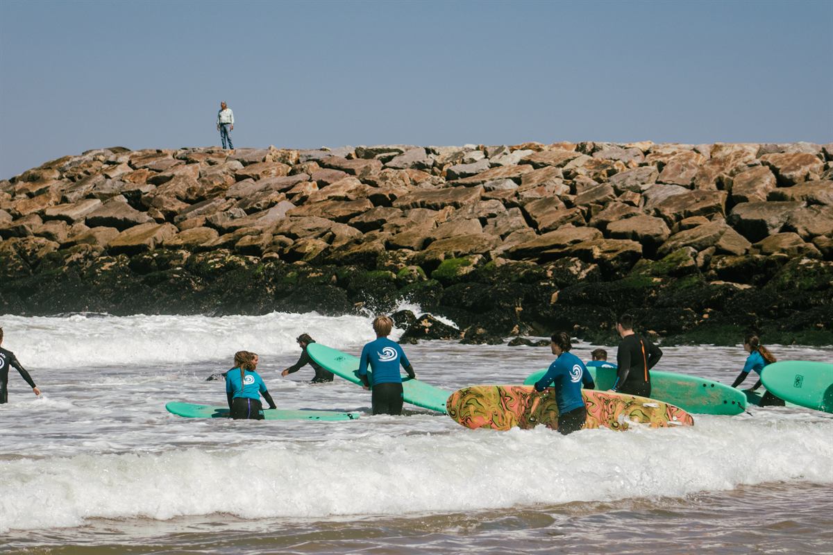 Grupo de alunos com pranchas na espuma, junto ao molhe
